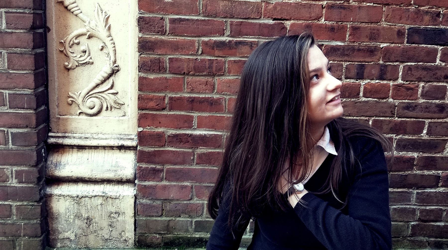 Carrie Callahan standing against brick wall staring to the right and smiling