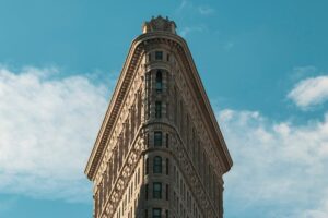 A flat iron shaped building against a partly cloudy blue sky